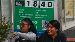 Mujeres sentadas afuera de un banco de compra y venta de dólares.