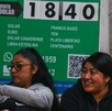 Mujeres sentadas afuera de un banco de compra y venta de dólares.