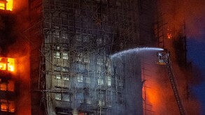 Edificios incendiándose junto a escalera con bomberos aventando agua
