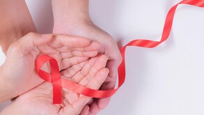 Una toma de estudio con las manos de una persona sosteniendo una cinta roja de concientización, doblada en forma de lazo.