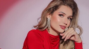 Isabel Zamora viendo de perfil con la mano apoyada sobre su mentón y usando un vestido rojo sobre un fondo rosa