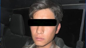 Se observa a un joven con camisa de cuadros café y con cintillla negra en los ojos.