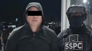 Hombre con sueter y gorro, línea negra en los ojos, elemento uniformado detrás de él