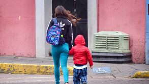 una mujer lleva a su hijo de la mano caminando en una calle