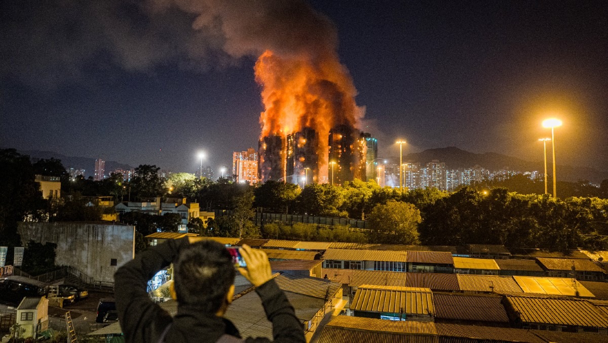 Joven sosteniendo un celular con un incendio de edificios de fondo