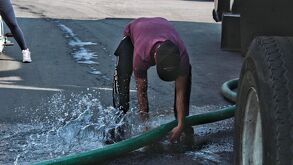 un hombre intenta conectar una manguera de agua a una pipa