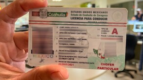 Se observa en la imagen una mano que agarra una licencia de conducir.