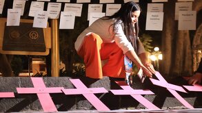 una mujer coloca veladoras cerca de cruces rosas alusivas a la violencia de género