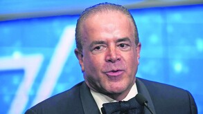 Primer plano de un hombre calvo, Raúl Cantú de la Garza (político), con traje y pajarita negra, hablando seriamente en un evento contra un fondo azul brillante