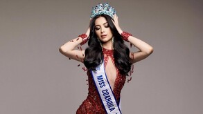 Se observa una mujer con una corona de diamantes, quien porta un vestido rojo.