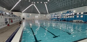 Se observa una alberca llena de agua con muchas sillas a los costados.