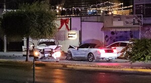Patrulla de Tlaquepaque de frente con las puertas abiertas y severos daños frente a auto marca Mustang deportivo descapotado en calles de Guadalajara