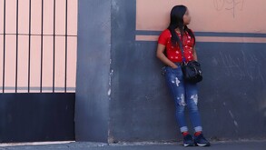 Una mujer vestida de rojo recargada sobre una pared de la calle 14 Poniente en Puebla.