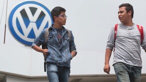 Dos hombres caminando delante de un logo de la armadora alemana de vehículos Volkswagen.