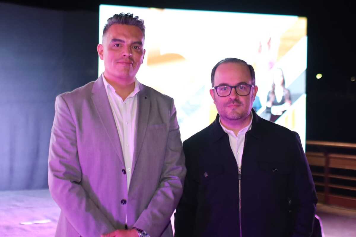 Ángel Carrillo y Alberto Braña posan para fotografía durante el 35 aniversario de Multimedios Laguna. Al fondo se ve la proyección de imágenes.