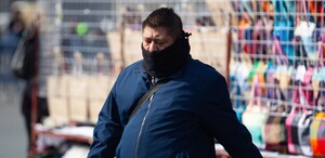 Se observa a un hombre con bufanda y chaqueta color azul caminando y con la mirada hacia abajo.