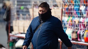 Se observa a un hombre con bufanda y chaqueta color azul caminando y con la mirada hacia abajo.