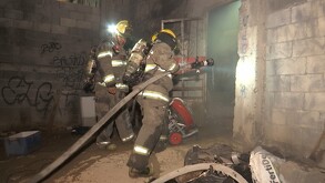 Se ven unos bomberos con mangueras en una casa con graffiti.