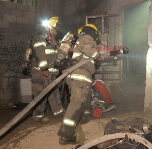 Se ven unos bomberos con mangueras en una casa con graffiti.