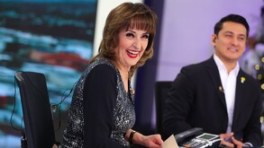 Se observa a una mujer sonriendo con una blusa gris con negro y de fondo se ve a un joven sonriendo de traje.