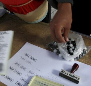 En la imagen se observa una hoja blanca, un sello y bolas balncas y negras.