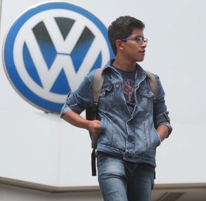 Dos hombres caminando delante de un logo de la armadora alemana de vehículos Volkswagen.