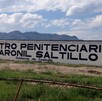 Hay una  barda pintada de blanco con letras que dicen Centro Penitenciario Varonil Saltillo.