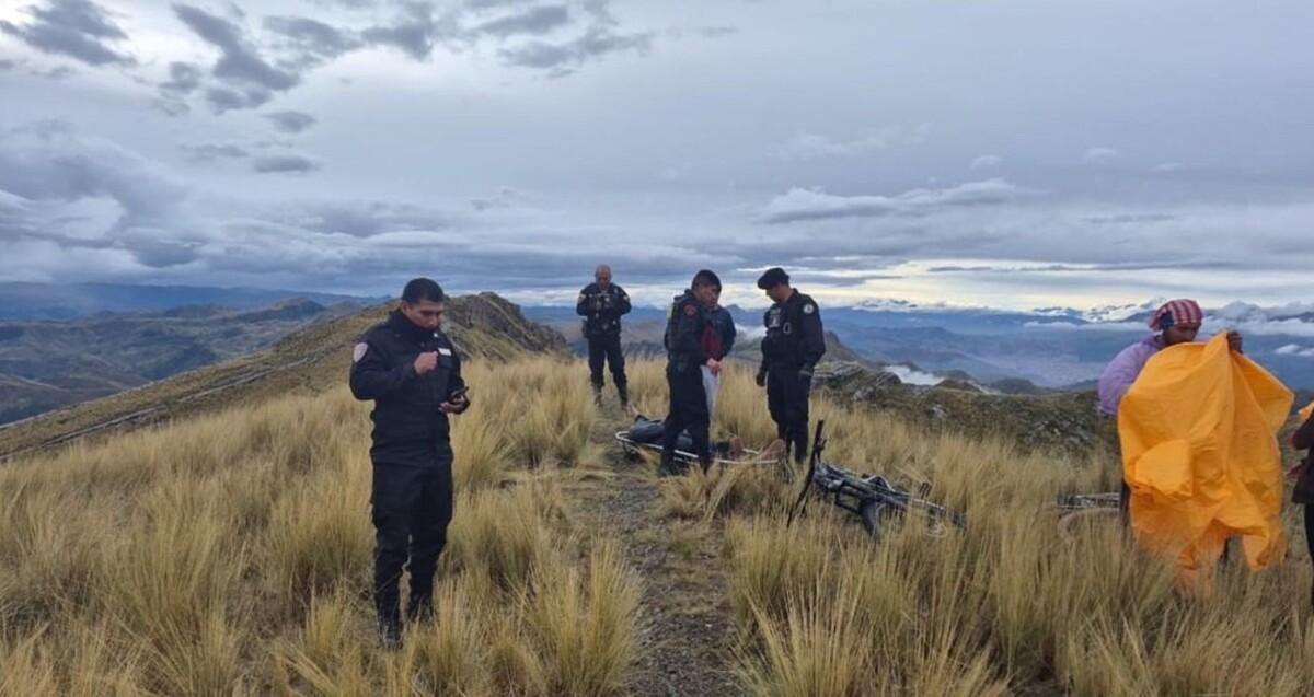 Policías de Perú en la cima de una montaña con un hombre en una camilla y una bicicleta tumbada en el suelo. A un lado un hombre sosteniendo tela amarilla