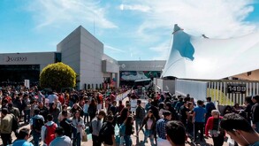 Una gran multitud de personas (visitantes de la FIL) afuera del edificio de la Expo Guadalajara bajo el sol. El edificio principal tiene una carpa blanca grande
