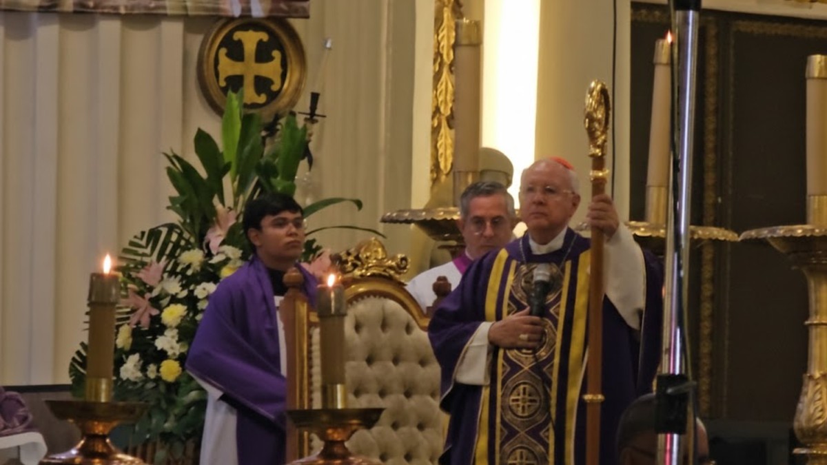Una vista trasera de una congregación sentada en una iglesia de estilo barroco. Un cardenal (de sotana morada) está de pie en el púlpito dando misa.