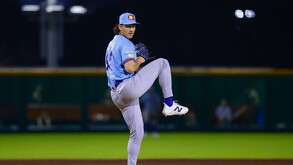 Un lanzador de béisbol de los Charros de Jalisco (uniforme azul claro y gorra azul) está en medio de su lanzamiento en un campo. El juego se lleva a cabo en la