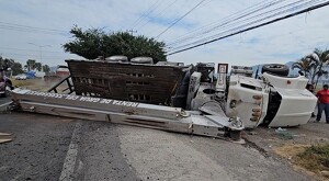 Grúa de color blanco volcado sobre su costado encima del asfalto de la carretera Guadalajara-Morelia con personas y vehículos alrededor