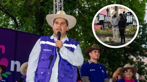 El político Carlos Manzo (con sombrero de paja y chaleco púrpura) habla en un micrófono en un evento al aire libre en un parque. Otros asistentes con sombreros
