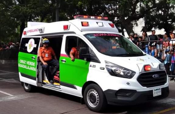 Ambulancia de la Cruz Verde de Guadalajara con las puertas abiertas y paramédicos en su interior con personas a un costado detrás de una valla de seguridad