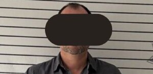 Se observa a un hombre con ojos tapados y vistiendo una playera color gris.