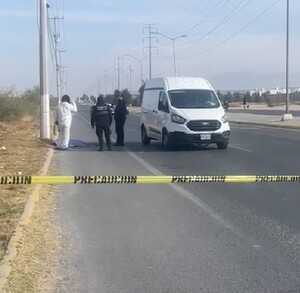 Se observa un hombre tendido en el suelo, una cinta de precaución amarilla y una camioneta blanca.
