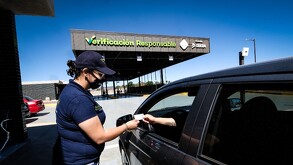Una mujer empleada en un centro de Verificación Vehicular recibe documentos de la mano de un conductor a través de la ventanilla de su coche.