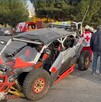 Se observa un RZr gris con rojo y jóvenes parados a lado de éste.