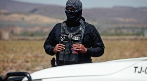 Oficial de la FGR con la cara cubierta por una pashmina frente a un campo y detrás de una camioneta blanca