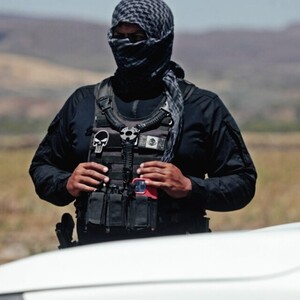 Oficial de la FGR con la cara cubierta por una pashmina frente a un campo y detrás de una camioneta blanca