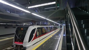 Un moderno tren del Tren Ligero de Guadalajara (blanco y rojo) espera en una estación subterránea limpia con pisos reflectantes, escaleras de mármol negro y luc