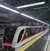 Un moderno tren del Tren Ligero de Guadalajara (blanco y rojo) espera en una estación subterránea limpia con pisos reflectantes, escaleras de mármol negro y luc