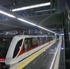 Un moderno tren del Tren Ligero de Guadalajara (blanco y rojo) espera en una estación subterránea limpia con pisos reflectantes, escaleras de mármol negro y luc