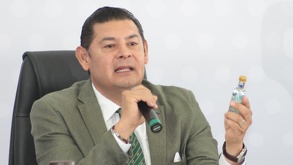 El gobernador de Puebla, Alejandro Armenta, con una botella de mezcal en la mano y una expresión firme.