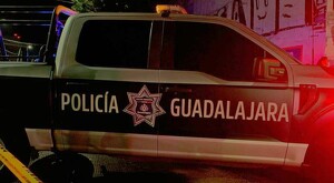 Vista del costado de una patrulla de la Policía Municipal de Guadalajara estacionada frente una pared con grafitis y una cinta policiaca amarilla detrás