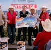 Esteban Villegas y Susy Torrecillas sonríen junto a productores recibiendo un vale de semilla de alfalfa. El vale es de tamaño grande y simbólico del apoyo.