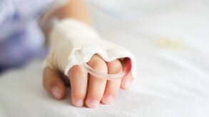 Se observa la mano de un niño que está en una cama como de hsopital.