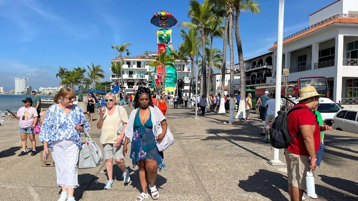 Tres mujeres (turistas) sonrientes examinan un expositor lleno de gafas de sol, sombreros y souvenirs artesanales en un mercado al aire libre de Puerto Vallarta