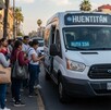Personas esperando para abordar una camioneta tipo van con el letrero de Huentitán en la parte superior