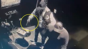 Un hombre con gorra y un arma en su mano, grabado con una cámara de seguridad.